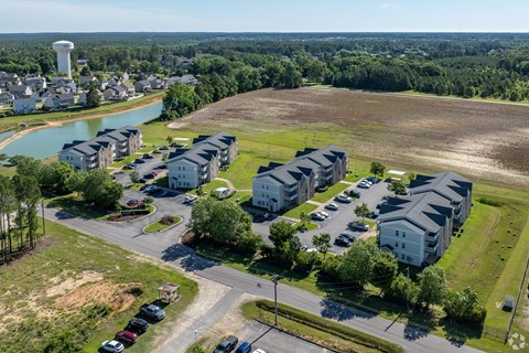 A bird's eye view of a residential area with apartment buildings, a parking lot, and a water body.