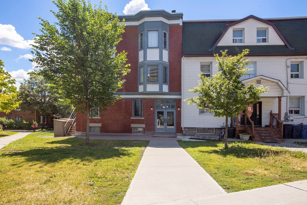 A red brick building with a white trim and a black roof sits next to a white house with a red roof.