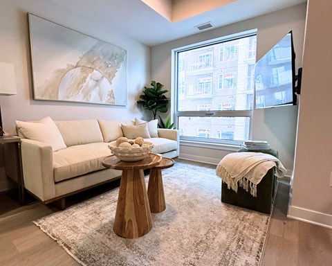 A living room with a white couch, a wooden coffee table, and a large window.