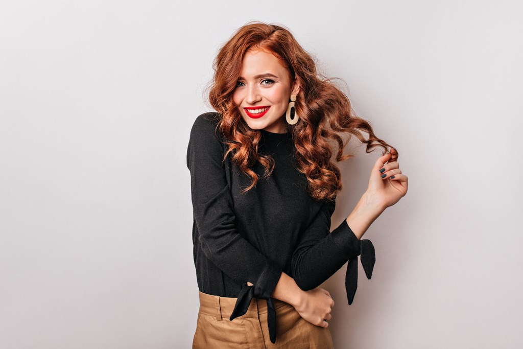 a young woman with red hair leaning against a white wall
