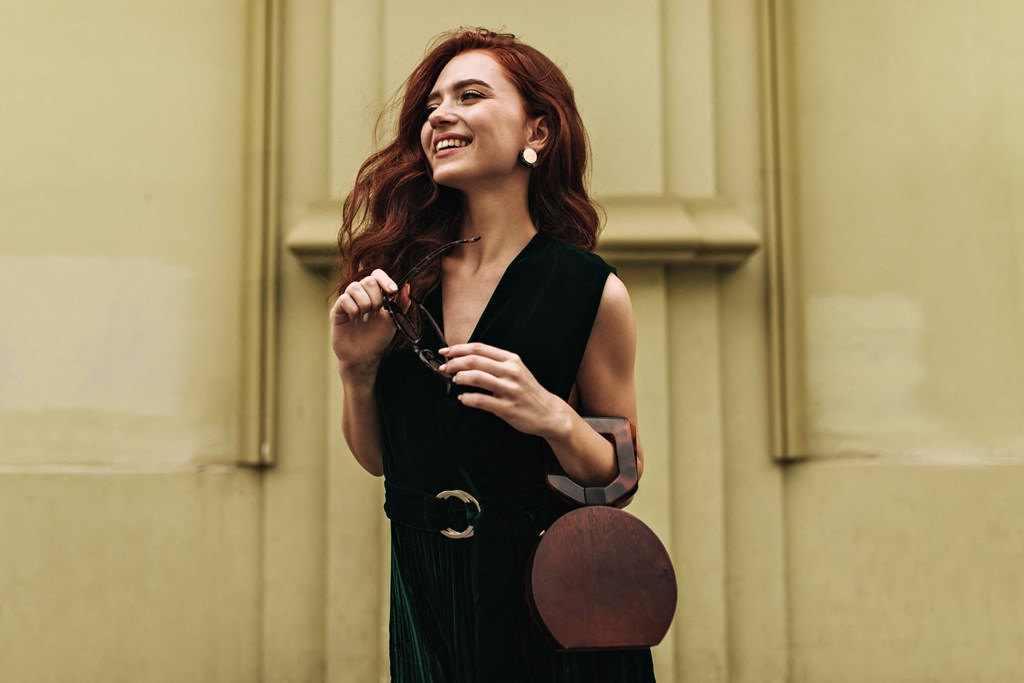 a woman in a black dress holding a brown purse and smiling