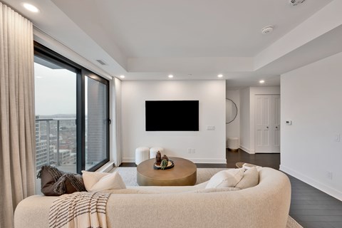 A modern living room with a large couch and a flat screen TV mounted on the wall.