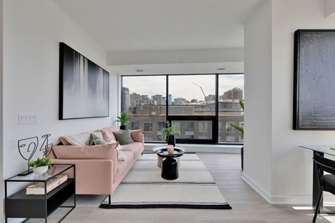 A modern living room with a pink couch and a large window overlooking the city.