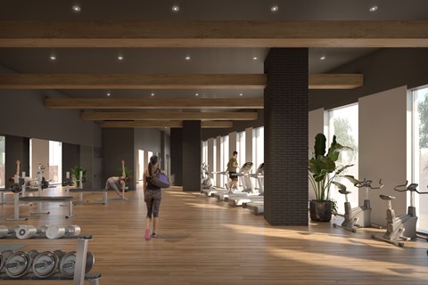 A woman is walking through a spacious gym with wooden floors and various exercise equipment.