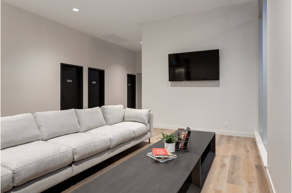 A white couch sits in a room with a black coffee table and a flat screen TV mounted on the wall.