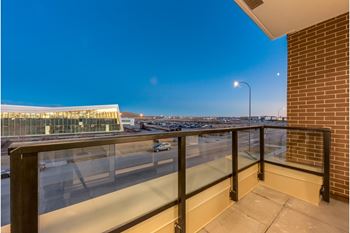 A balcony with a glass railing overlooking a parking lot and a building.
