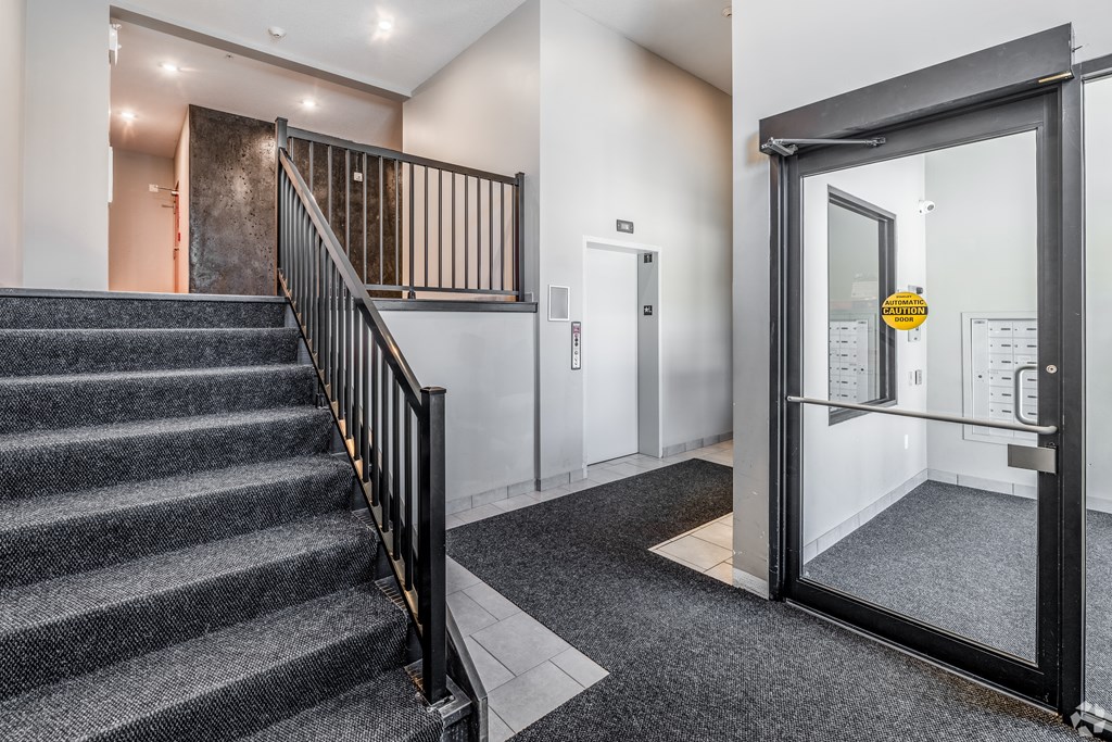 A staircase with a black railing leads to a door with a yellow sign on it.