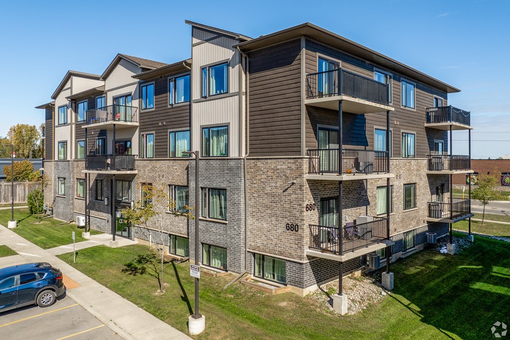A modern apartment building with balconies and a car parked in the driveway.