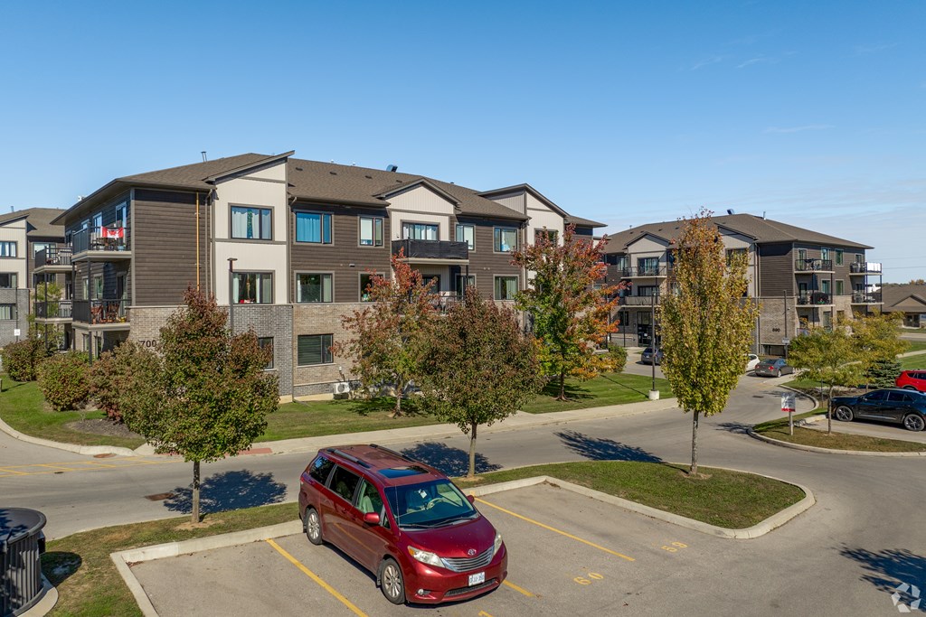 A red car is parked in a parking lot in front of apartment buildings.