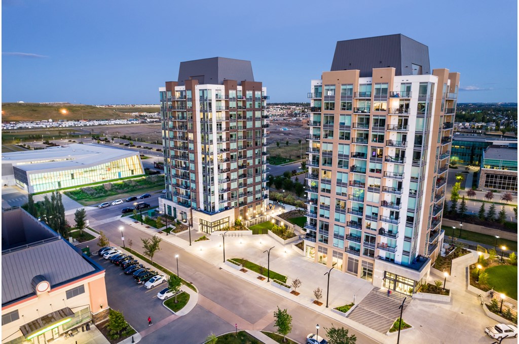 Two modern high-rise buildings are surrounded by a parking lot and other buildings.