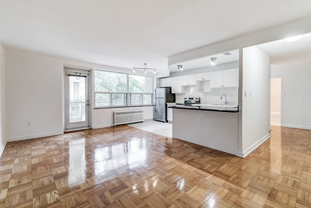 an empty living room with a kitchen and a large window