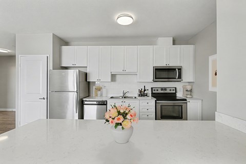 A kitchen with white cabinets and appliances, a marble countertop, and a vase of flowers on the counter.