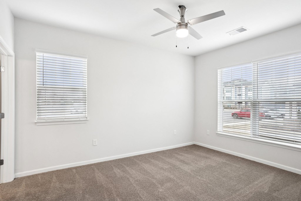 A room with a ceiling fan and two windows with blinds.