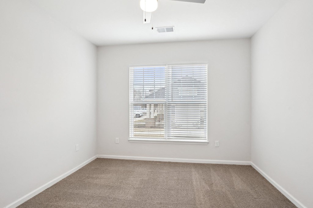 A room with a carpeted floor and a window with blinds.