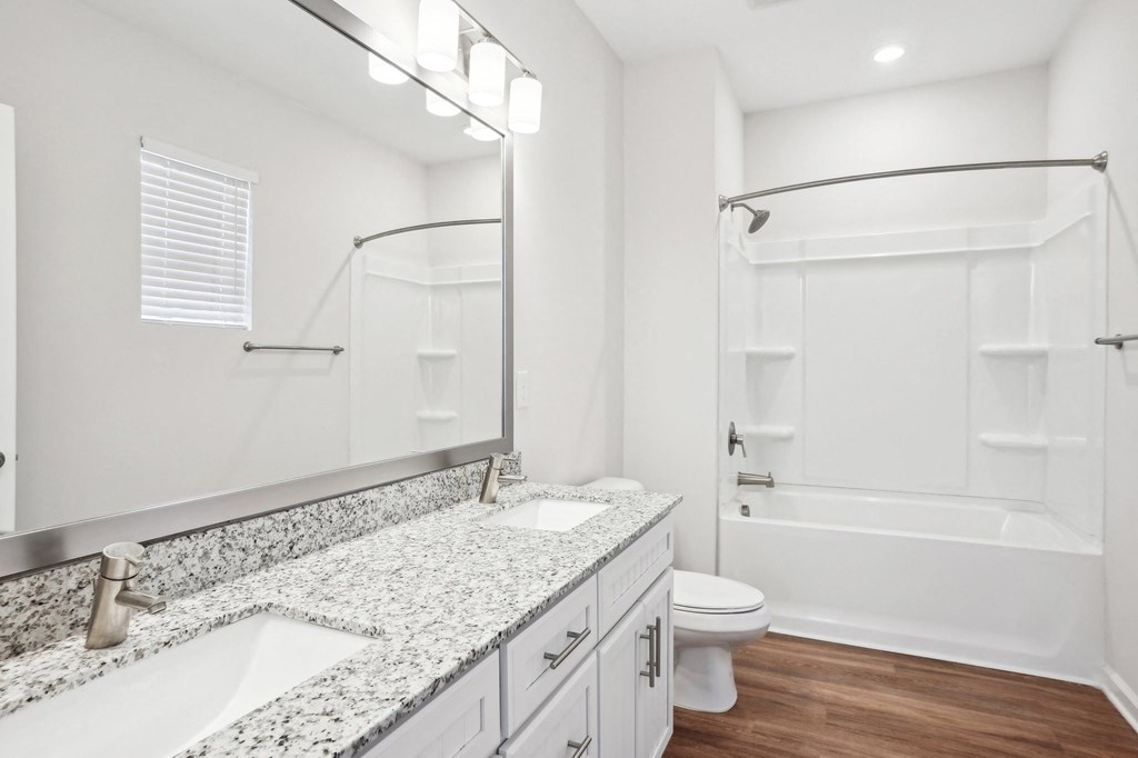 A white bathroom with a granite counter top and a walk-in shower.