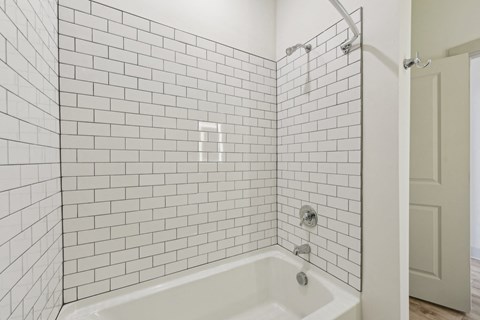 A white tiled bathroom with a white tub and shower.
