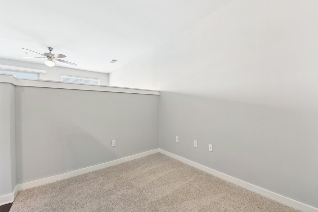 A room with a carpeted floor and a ceiling fan.