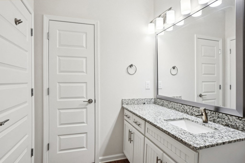 A bathroom with a white door, a marble countertop, and a mirror with lights.