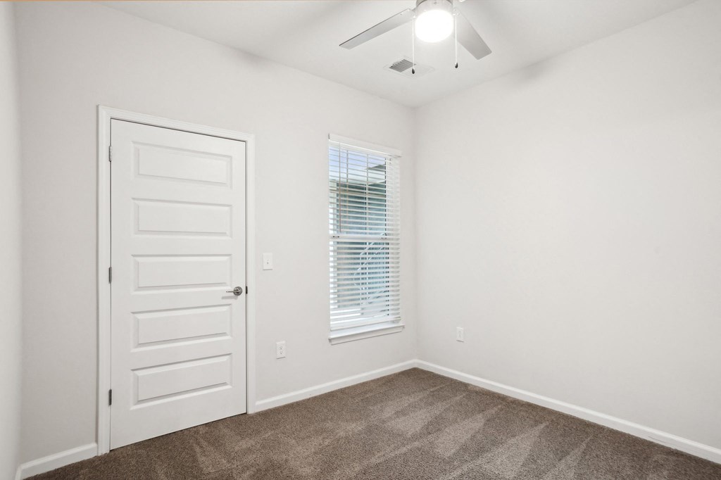 A room with a carpeted floor, a white door, and a window with blinds.