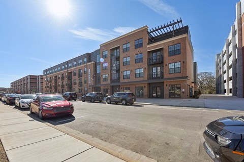A sunny day at a parking lot with cars and apartment buildings.