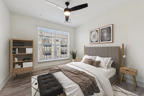 A bedroom with a large bed, a ceiling fan, and a window with blinds.