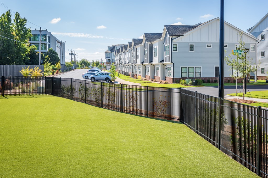 A black fence surrounds a green lawn in front of a row of houses.