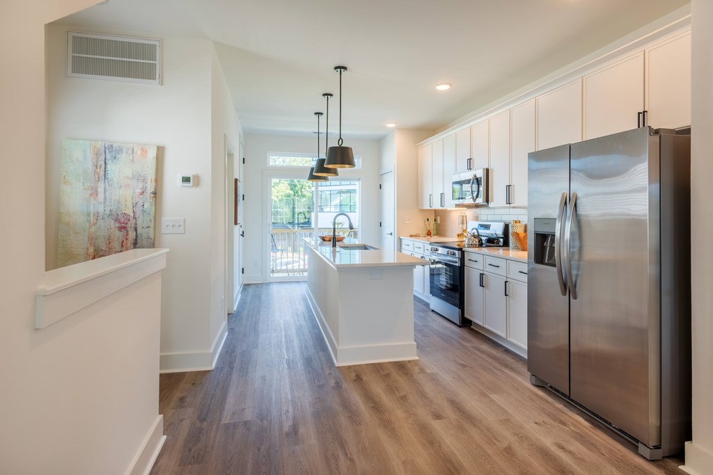 A modern kitchen with a refrigerator on the right and a dining area in the background.
