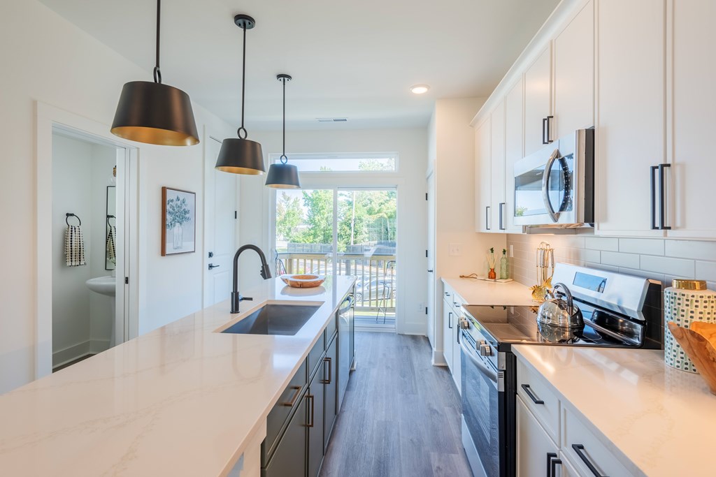 A kitchen with a white counter top and black pendant lights.