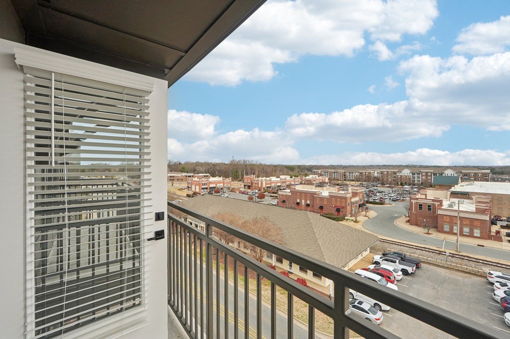 A balcony with a view of a parking lot and buildings.