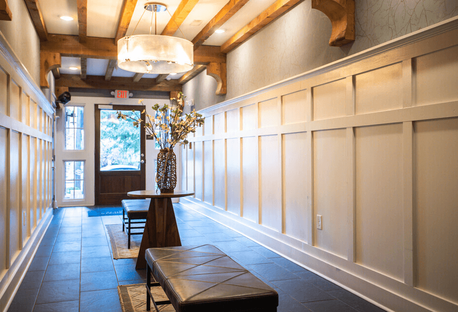 A long hallway with a bench and a vase on a table.