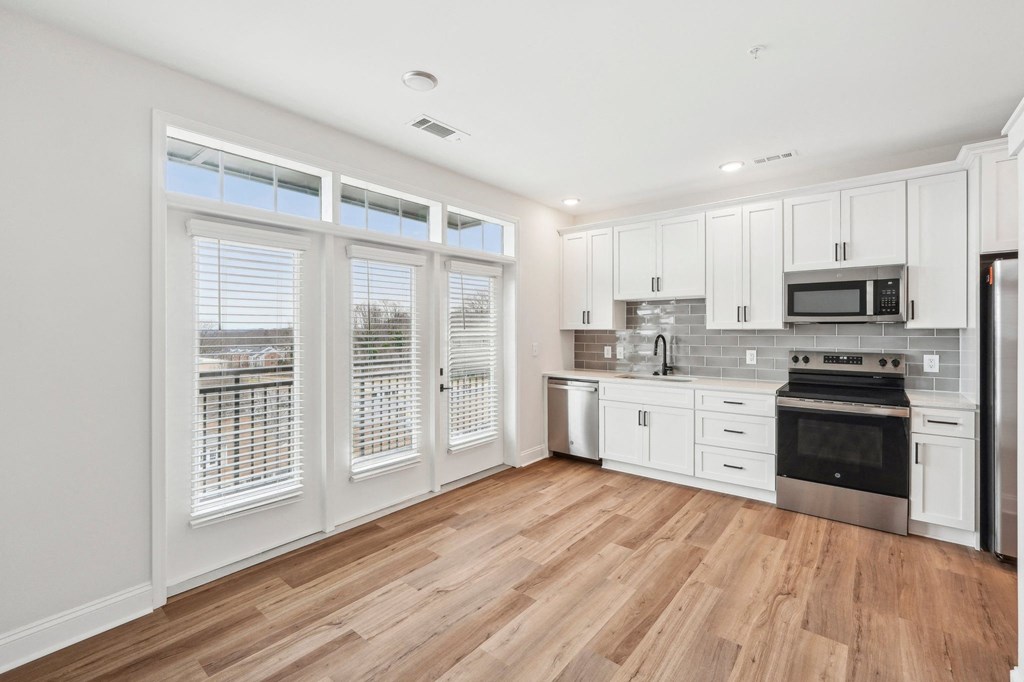 A kitchen with white cabinets and a wooden floor.