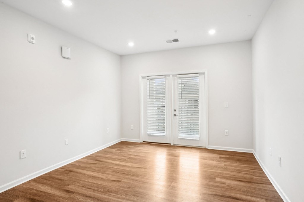 A room with wooden flooring and a white door with blinds.