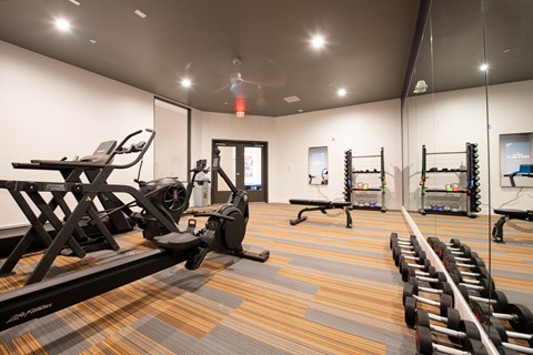 a gym with cardio equipment and weights on the floor and a mirrored wall