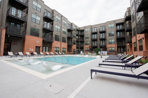 a swimming pool with lounge chairs in front of an apartment building