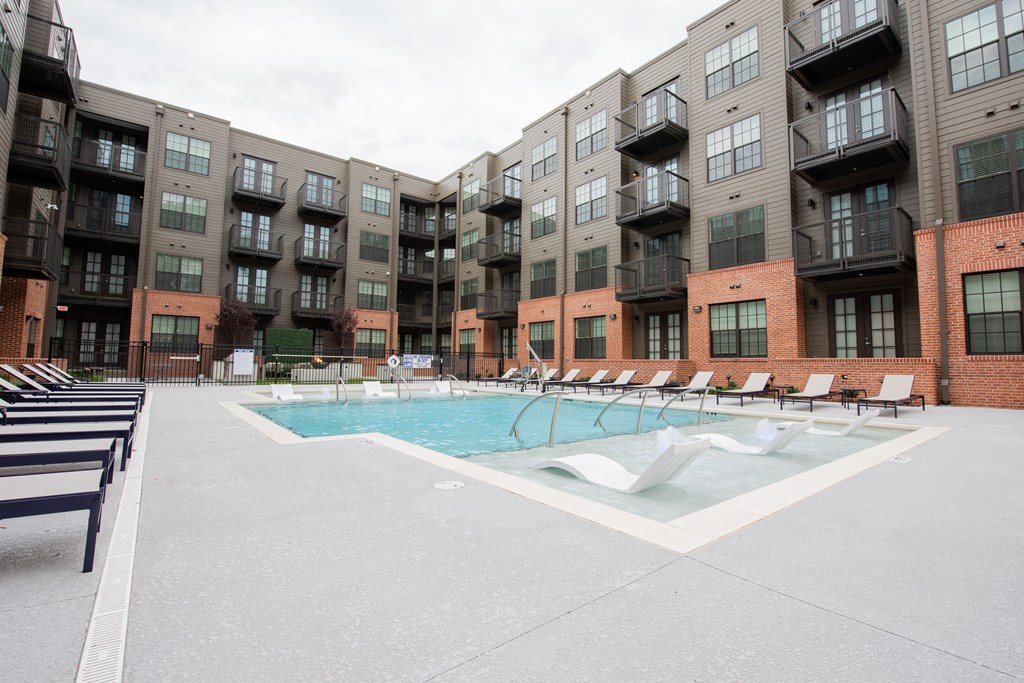 a swimming pool with chairs in front of an apartment building