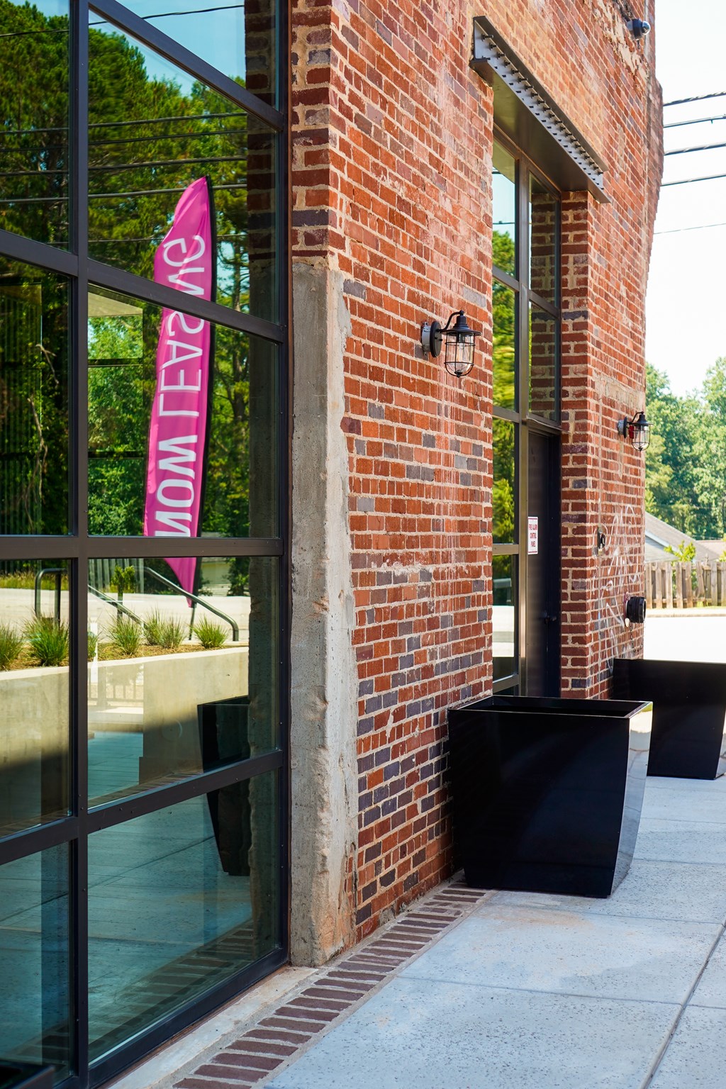 A red brick building with a glass door and a pink banner that says "Sunset Women".