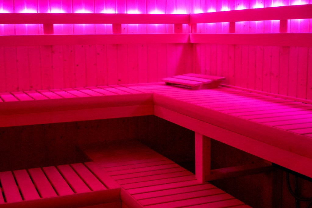 A pink lit room with a bench in the middle.
