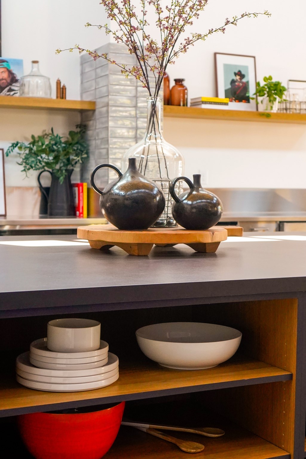 Two black vases on a wooden stand with a plant in the middle.