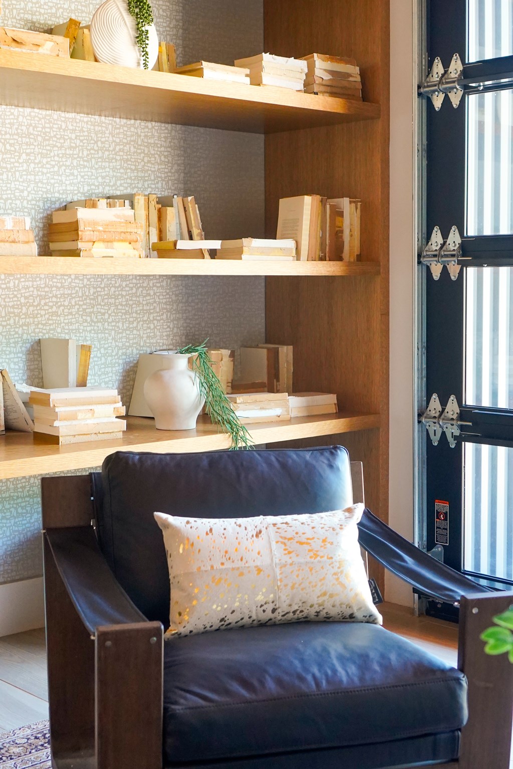 A black leather chair with a white pillow and a shelf with decorative items.