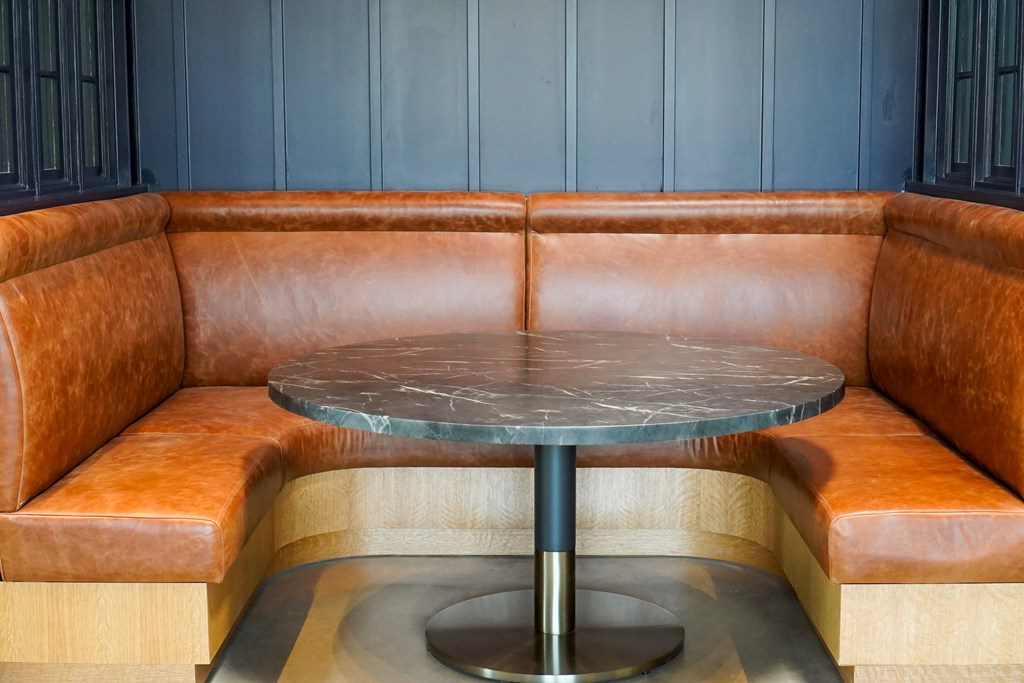 A round table with a metallic base is surrounded by brown leather seating.