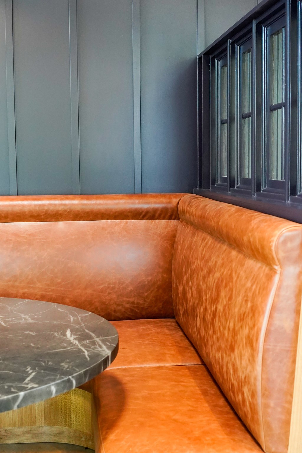 A brown leather sofa with a grey marble table in front of it.