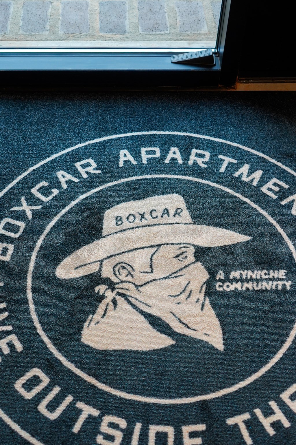 A rug with a cowboy on it and the words "Boxcar Apartments" written on it.