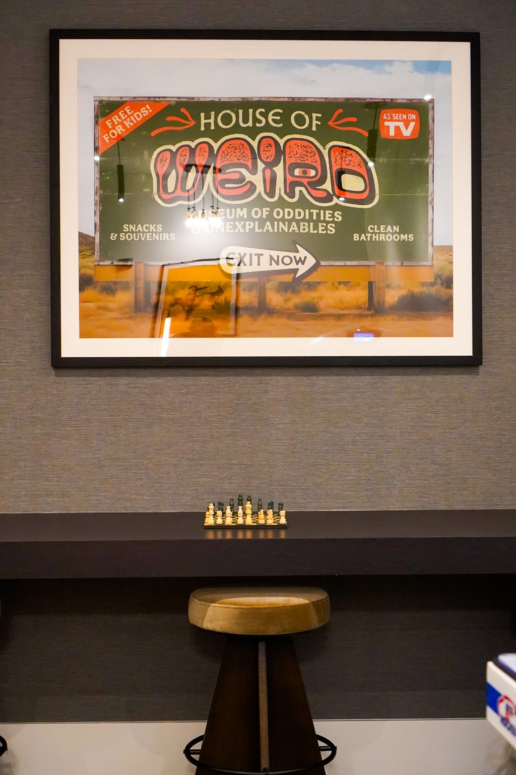 A framed poster of House of Weird is hanging on the wall above a bar stool.