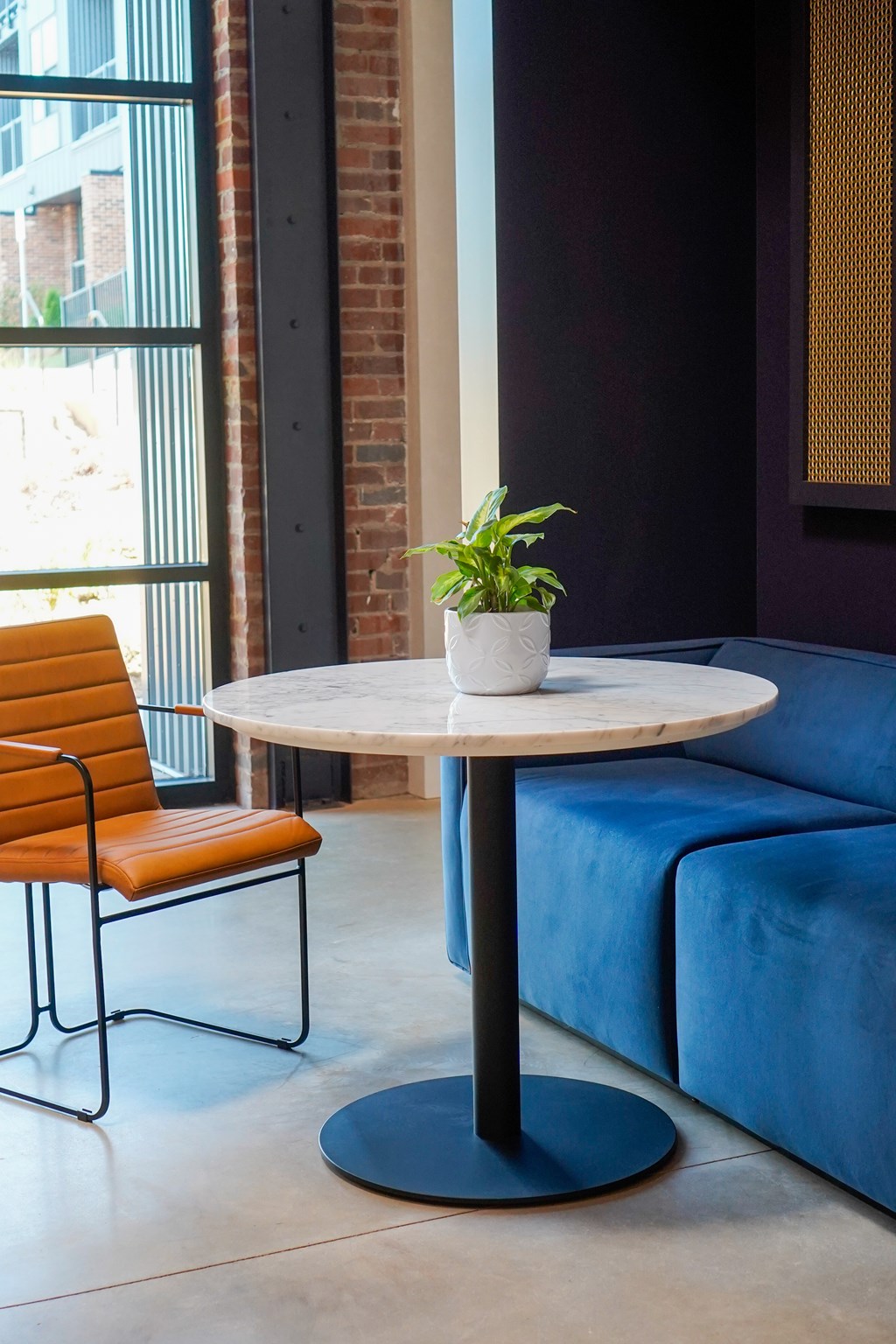 A round table with a plant on it sits between a blue couch and a chair.