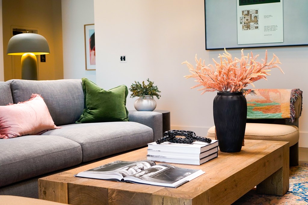 A grey couch with a green pillow and a vase with orange flowers on a wooden table.