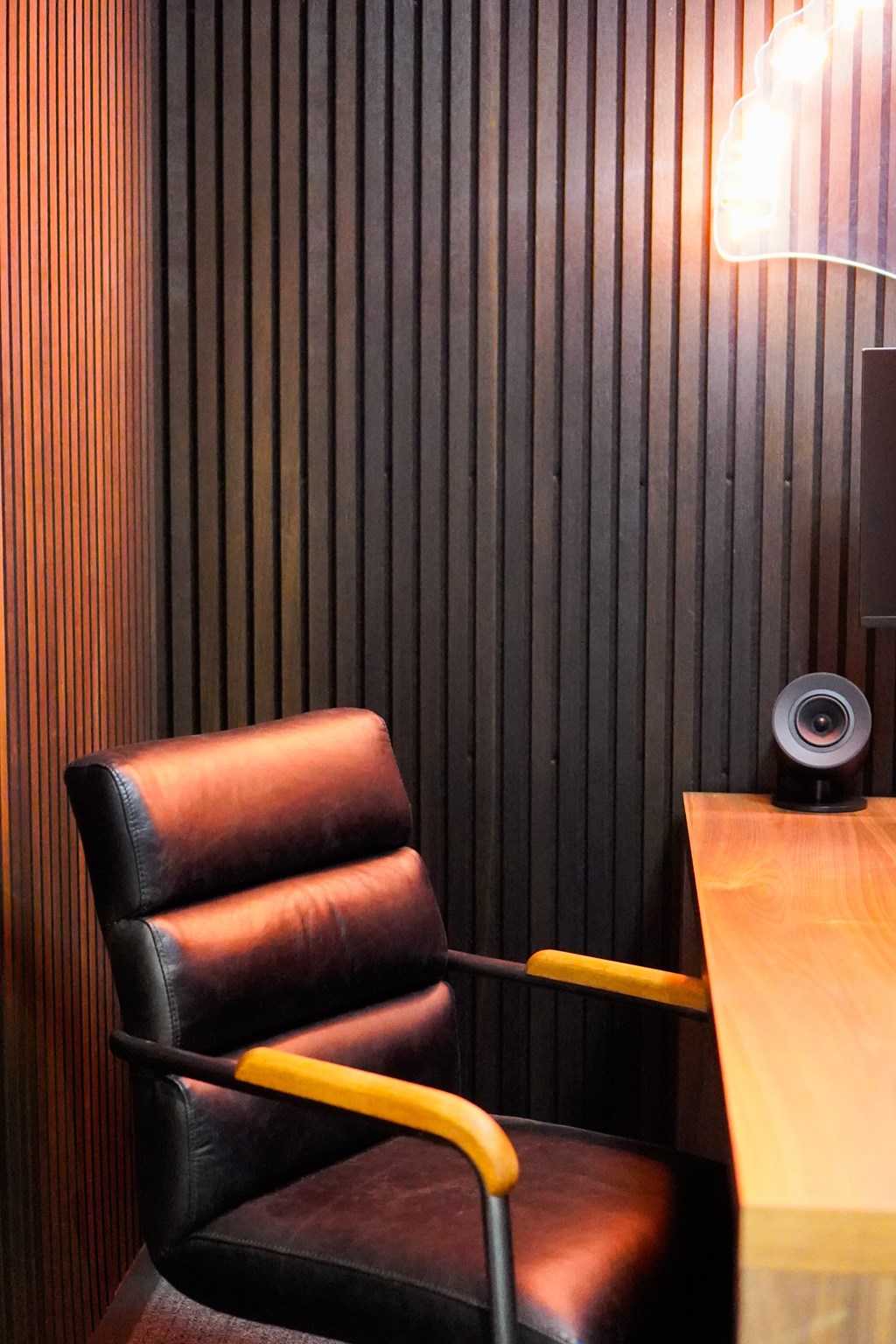 A black leather chair with a yellow armrest sits in front of a wooden desk with a speaker on it.