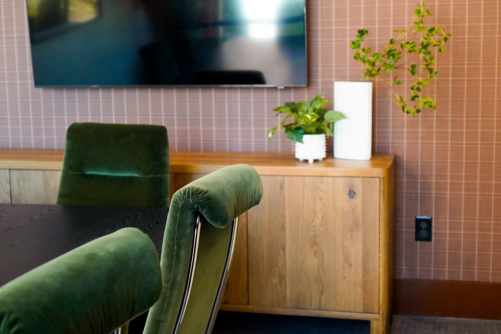 A green chair sits in front of a wooden cabinet with a plant on top.