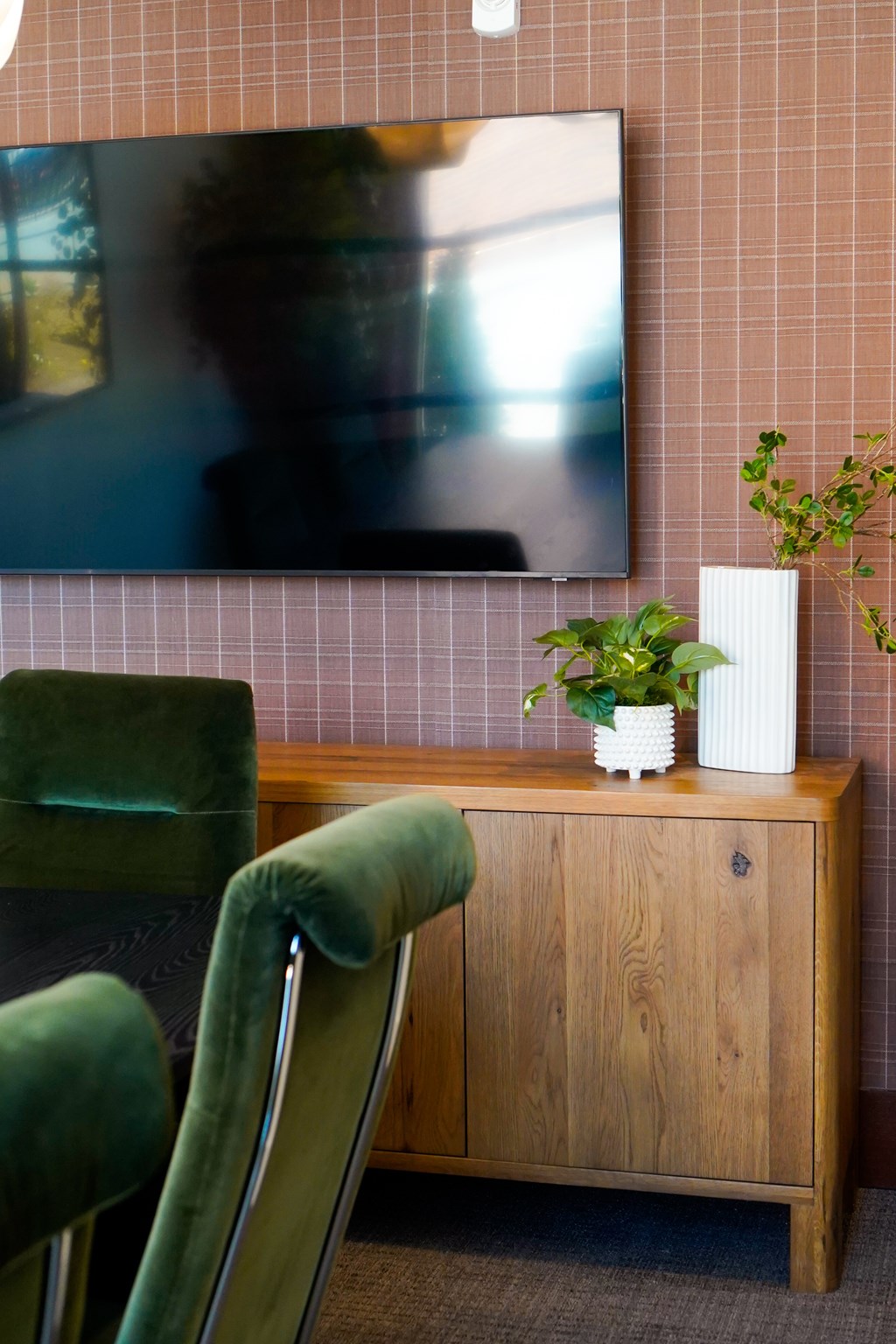 A green chair sits in front of a wooden cabinet with a television mounted on the wall behind it.