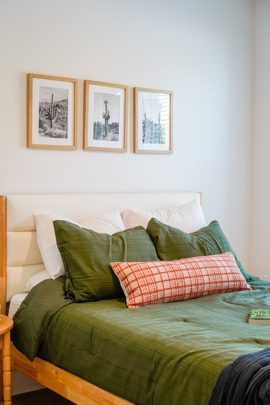A bed with a green comforter and pillows in front of a white wall with three pictures hanging on it.