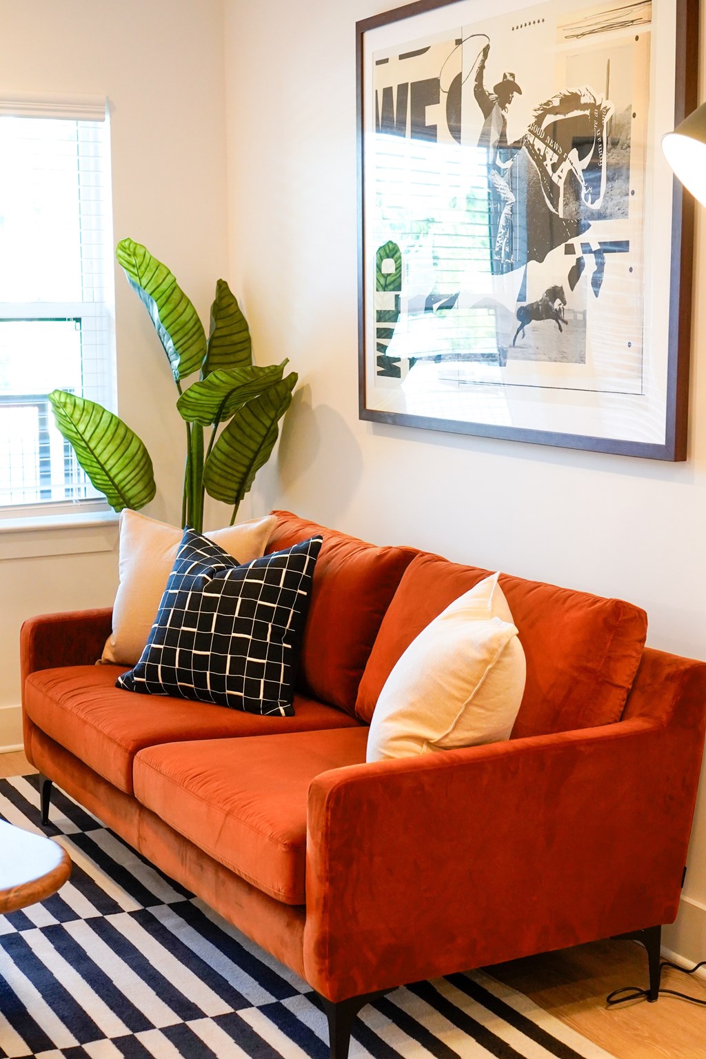 A red couch with a checkered pillow and a plant in a living room.
